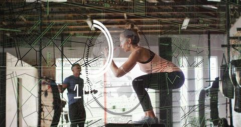 Female athlete performing plyo box jump with futuristic hud overlay in industrial gym