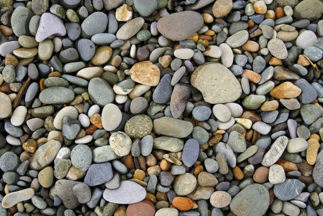 A diverse collection of colorful, smooth river pebbles. This arrangement of stones offers a natural background suitable for use in design projects, presentations, or as a backdrop for websites. The assorted colors and textures provide visual interest and are ideal for nature themes, geology, or relaxation materials.