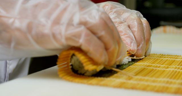 Close-up of hands in gloves rolling sushi using a bamboo mat in kitchen. Perfect for culinary websites, cooking blogs, Japanese cuisine presentations, professional culinary training materials, and modern dining advertisements.