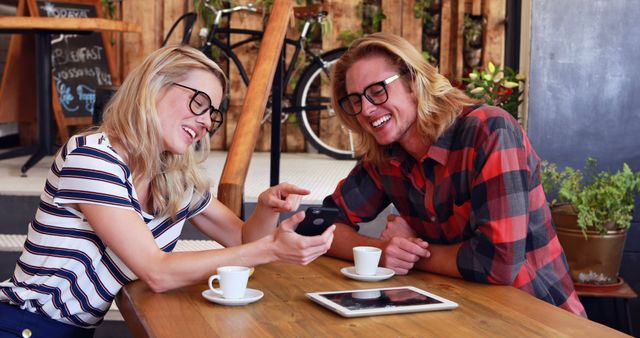 Friends laughing and looking at phone in cozy café - Download Free Stock Images Pikwizard.com