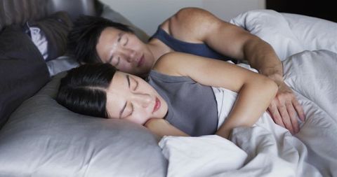 Asian couple cuddling and sleeping together in cozy bed with soft pillows and white duvet