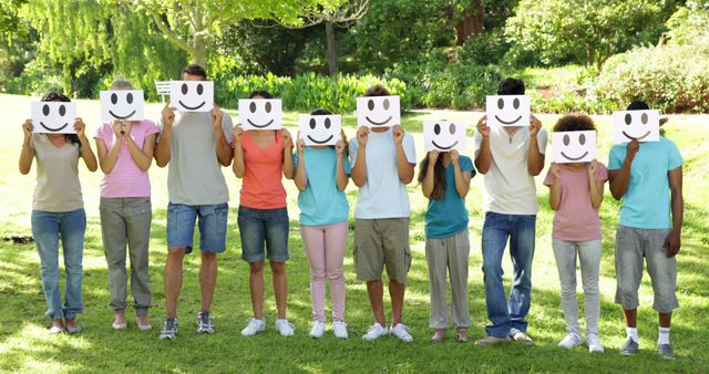 Group of casual young friends holding smiley faces over their faces on a sunny day