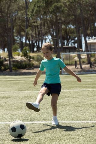Young girl kicking soccer ball on sunlit turf for youth sports practice and active play
