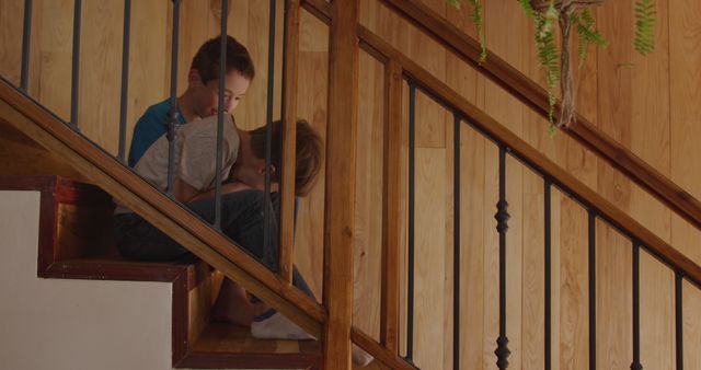 Happy caucasian brothers sitting on stairs and using smartphone at home. Technology, domestic life, childhood and lifestyle, unaltered.