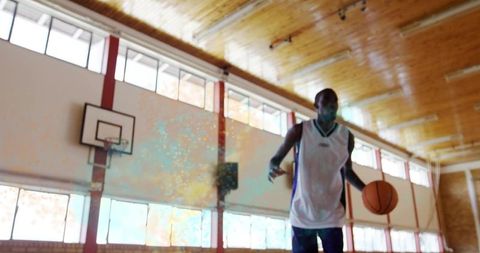 Masked basketball player dribbling on sunlit indoor court with copy space