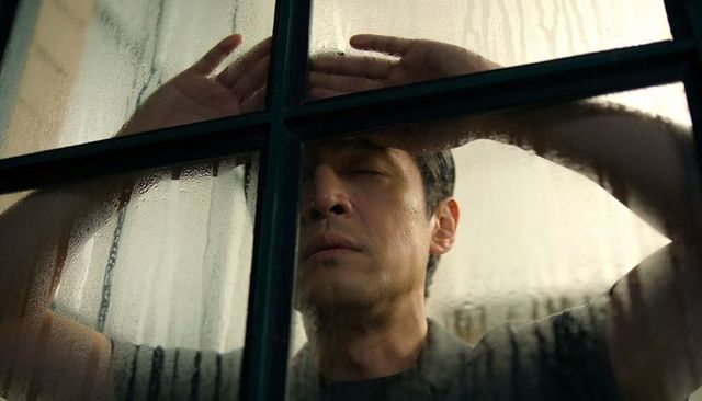 Contemplative man leaning against wet paned window pressing hands and forehead, portrait