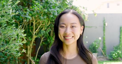 Smiling Asian Woman Relaxing in Sunlit Backyard