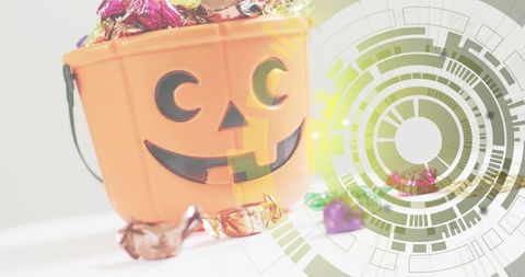 Overflowing jack-o'-lantern bucket spilling foil candies on white table with green circular overlay