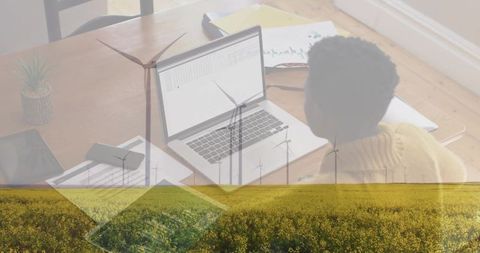 Black woman working on laptop with wind turbines double exposure for sustainable energy