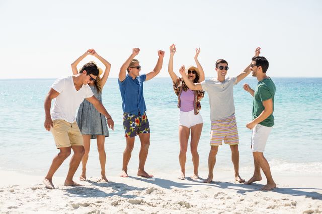 Group of young friends dancing and enjoying a sunny day at the beach. Perfect for use in advertisements, travel brochures, social media posts, and lifestyle blogs promoting summer activities, vacations, and outdoor fun.