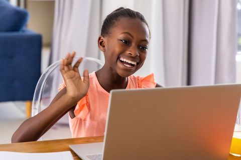 Smiling teenage girl waving during online video call at home with laptop