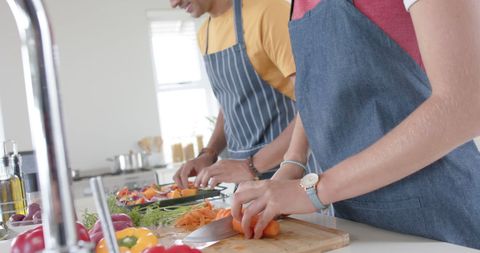 Couple Cooking Fresh Vegetables in Kitchen Together Wearing Aprons