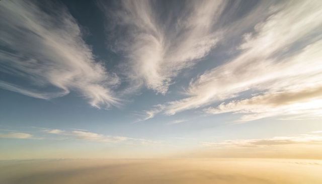 Cirrus clouds fanning across pastel sky over low misted horizon at golden sunrise