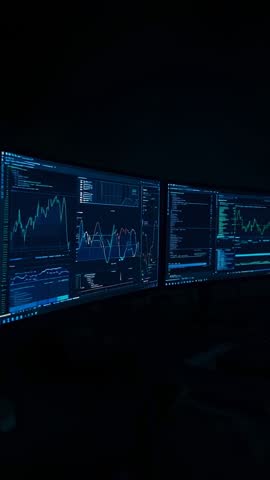 Panning across triple monitors showing live code, charts and data analytics in dark vertical video