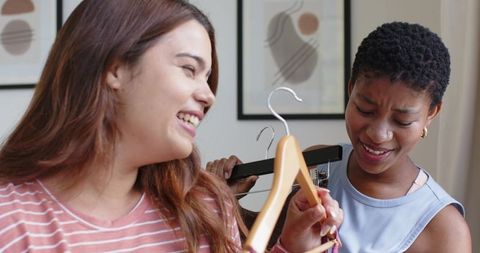 Friends comparing outfits and laughing while choosing clothes in casual cozy home wardrobe