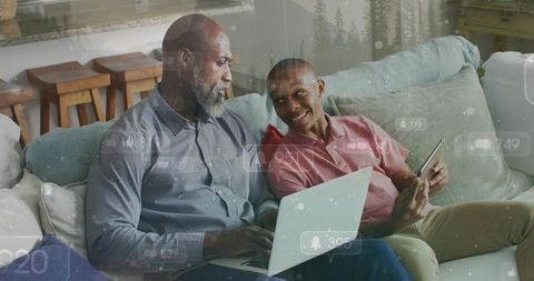 Father and teen son sharing laptop and smartphone on couch, smiling and connecting
