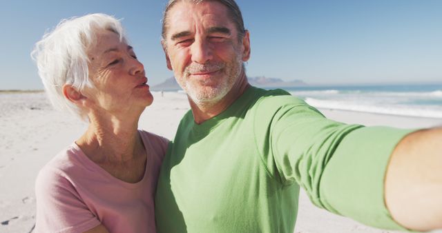 Senior couple taking selfie on beach during sunny day. Older adults smiling and enjoying each other's company on vacation, capturing memories by the ocean. Perfect for vacation advertising, mental and physical wellbeing promotions, retirement planning materials, and travel agency content.