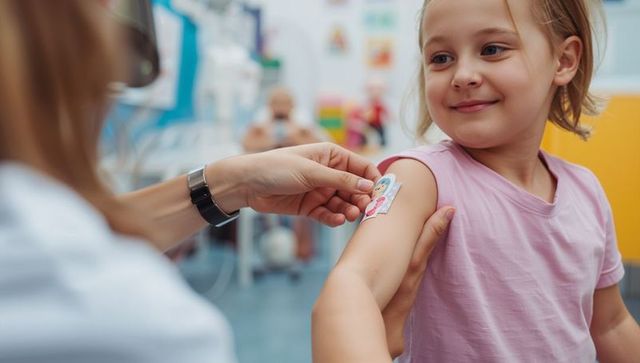 Nurse applying colorful bandage on smiling girl arm during pediatric clinic visit