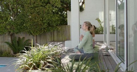 Women practicing outdoor yoga meditation on sunlit wooden deck calm wellness and mindfulness