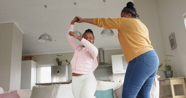 Mother and daughter enjoying time together dancing in living room. They are both smiling and seem to be having fun. Perfect for illustrating family bonding, joy, and quality time spent at home. Ideal for advertisements, lifestyle blogs, and parenting articles.