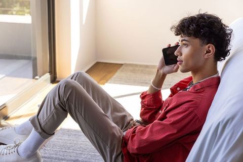 Young urban male relaxing while discussing on smartphone indoors