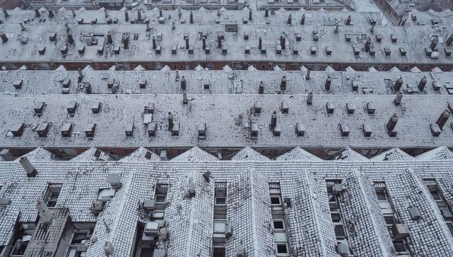 Aerial view of snowy tiled rooftops forming geometric grid with chimneys and skylights