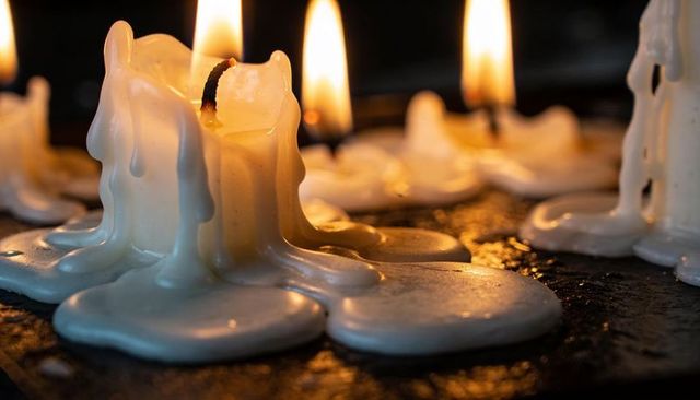 Melting White Candle with Dripping Wax and Warm Flame on Glossy Dark Tray