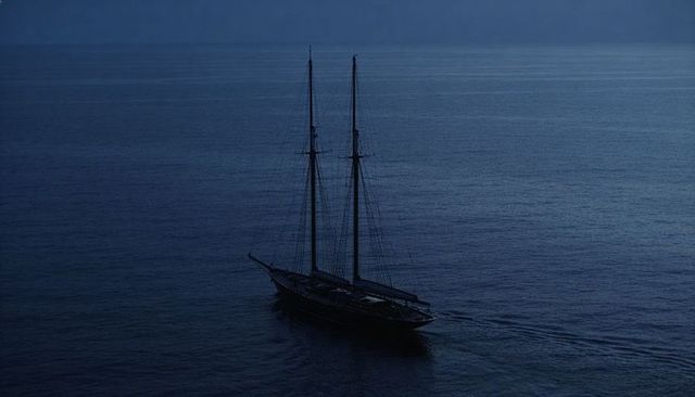Gliding two-masted schooner across twilight sea silhouette with quiet wake and tall masts