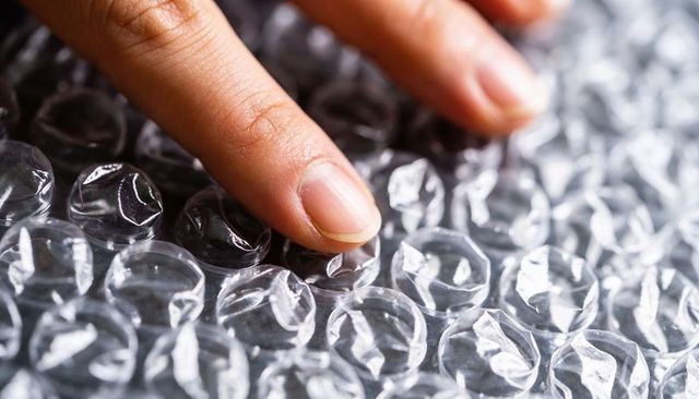 Index fingertip pressing bubble wrap sheet popping bubbles close-up tactile stress relief