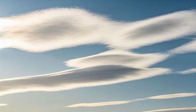 Elongated lenticular clouds drifting across pale blue sky with wispy high-altitude layers