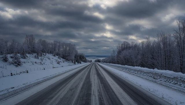 Long snow-covered highway stretching through winter countryside under overcast sky