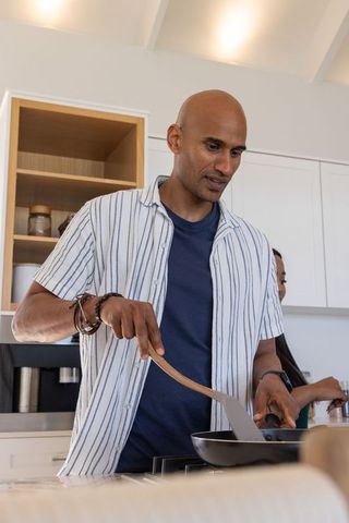 Man cooking in modern minimalist kitchen using wooden spatula and skillet, casual lifestyle