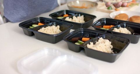 Preparing healthy meal prep containers with rice and fresh vegetables on countertop