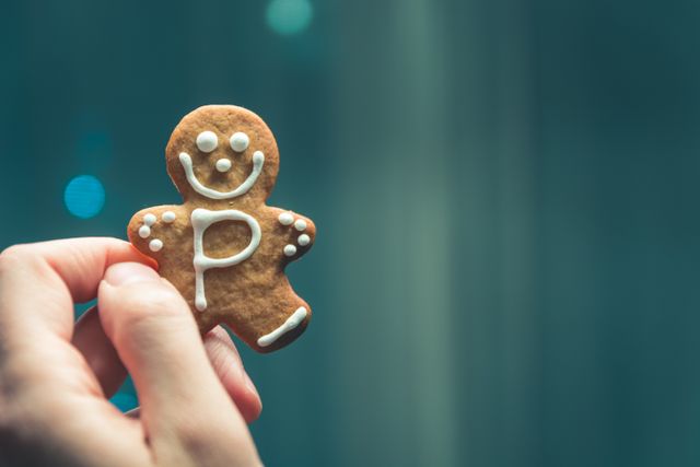 Hand holding gingerbread cookie decorated with smiley face and icing. Perfect for holiday season marketing, festive food blogs, Christmas recipes, and baking tutorials.