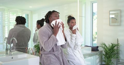 African american couple drying faces in bathrobes at sunlit modern double vanity bathroom