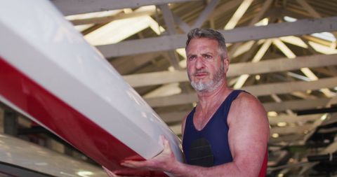 Senior man carrying rowing boat in boathouse