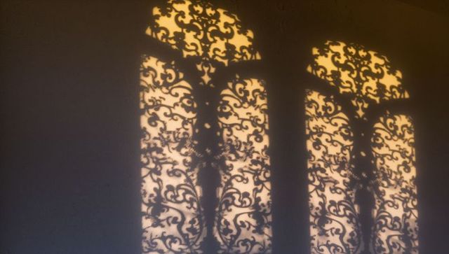 Sunlit arched grille shadows casting ornate scrollwork pattern on plaster wall