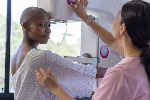 Diverse woman undergoing mammogram, technician adjusting equipment and supporting patient