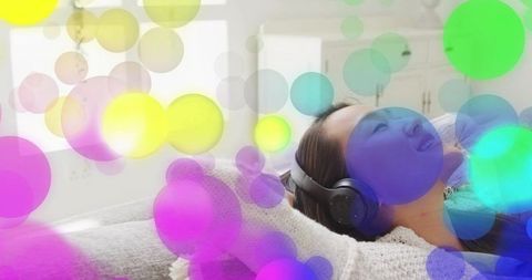 Relaxing woman listening with headphones on cozy sofa with colorful bokeh overlays
