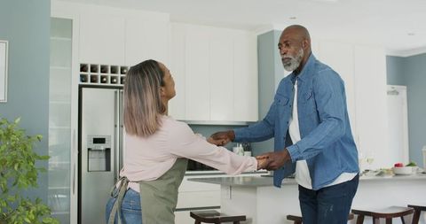 Mature black man and partner dancing in modern open-plan kitchen while holding hands