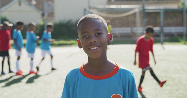 Young boy smiling confidently during soccer practice on a sunny day. Ideal for content promoting youth sports, outdoor activities for children, teamwork, health, fitness and summer recreation. Can also be used in educational and motivational materials related to child development and sportsmanship.