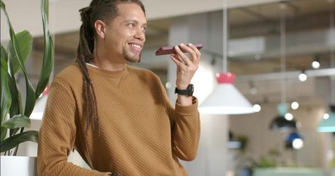 Recording voice message on smartphone in modern coworking space with plants and smartwatch