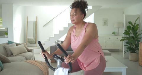 Woman pedaling on stationary bike in bright modern minimalist living room home workout