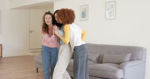 Multiracial friends embracing and laughing while leaning together in cozy living room