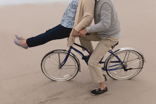 Senior couple enjoying a fun ride on a bicycle at the beach. Ideal for illustrating active retirement, healthy living, and outdoor leisure activities. Perfect for use in advertisements, brochures, and articles focused on senior lifestyle, travel, and wellness.