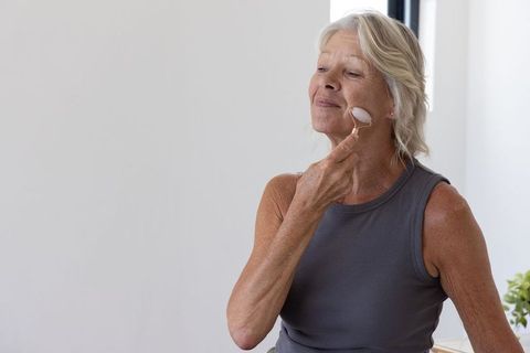 Senior woman using facial roller for at-home skincare routine, embracing calm wellness