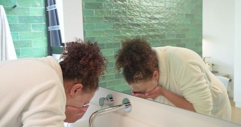 African american woman washing face at bathroom sink reflecting in mirror morning routine