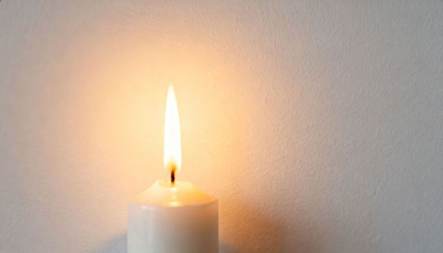 Burning white pillar candle casting warm glow on textured plaster wall for cozy mood