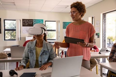 Diverse students exploring virtual reality while teacher guiding with tablet in classroom