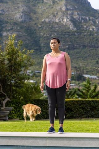 Mature woman standing at pool edge wearing pink top and leggings with golden retriever
